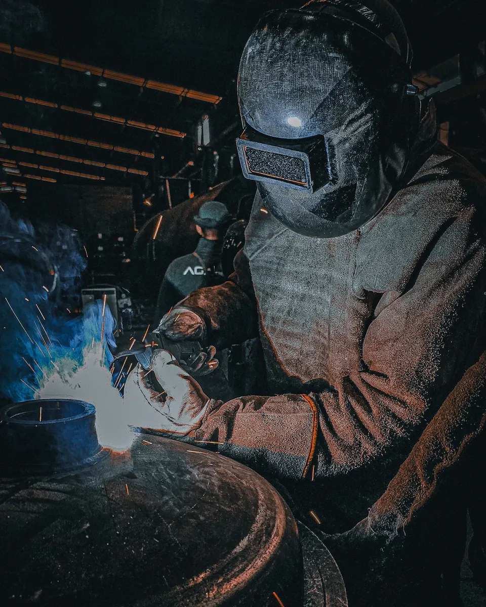 Soudeur casqué travaillant sur une pièce cylindrique dans un atelier