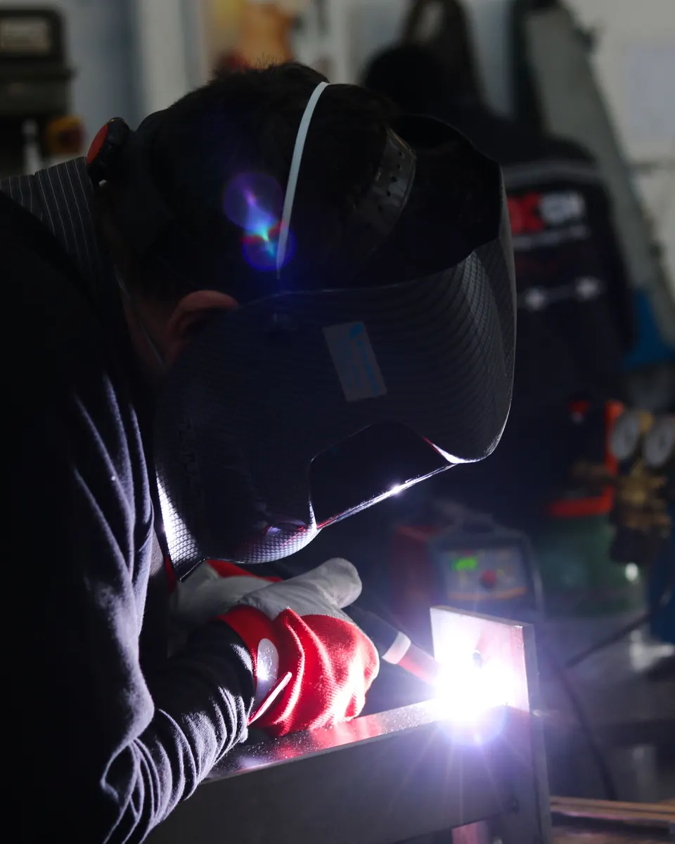 Soudeur au travail en soudure TIG sur une pièce métallique, éclairé par l'arc