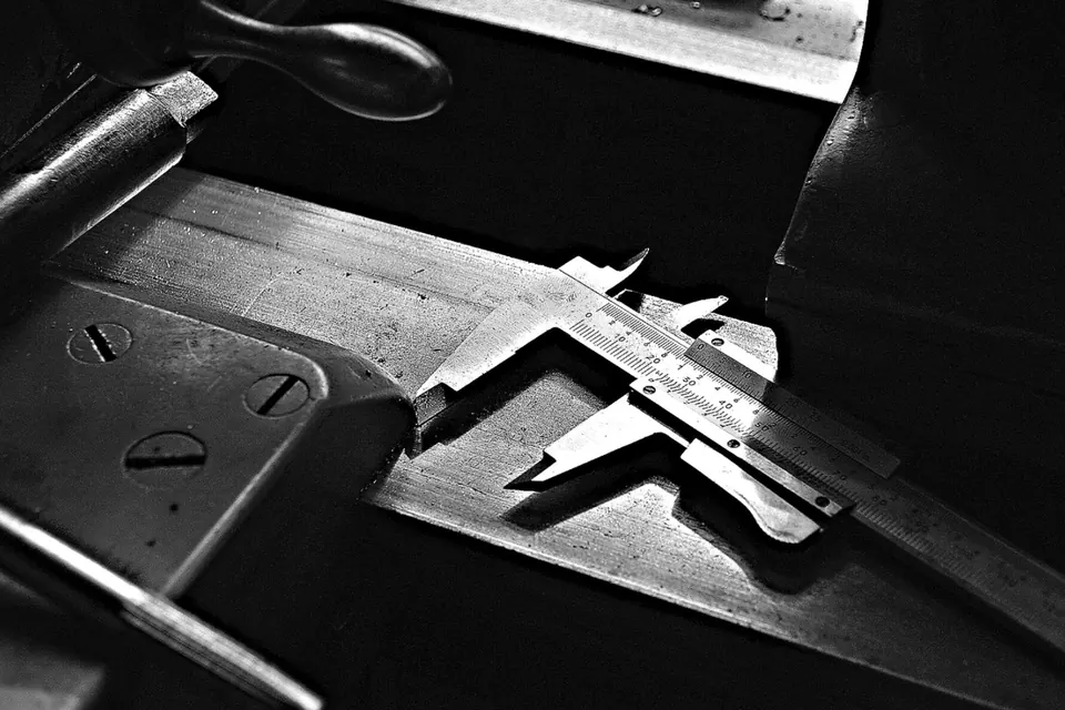 Pied à coulisse posé sur une pièce métallique, en noir et blanc